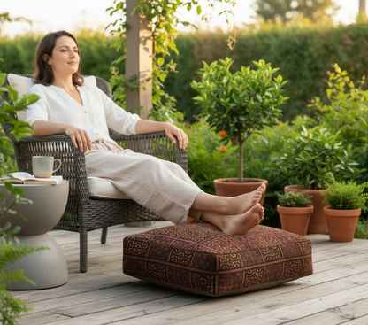 view of moroccan vintage rug pouf terracotta red used footrest on garden decking