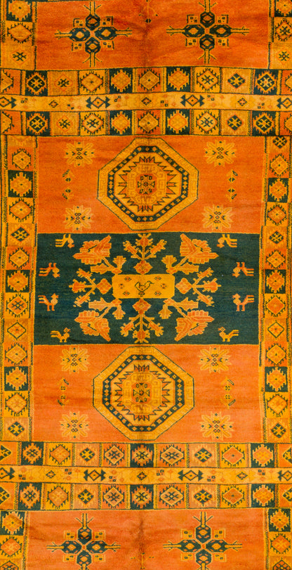 A square vintage rug with a traditional geometric pattern, featuring a dominant orange field, a central dark teal-blue band, and yellow/gold accents.