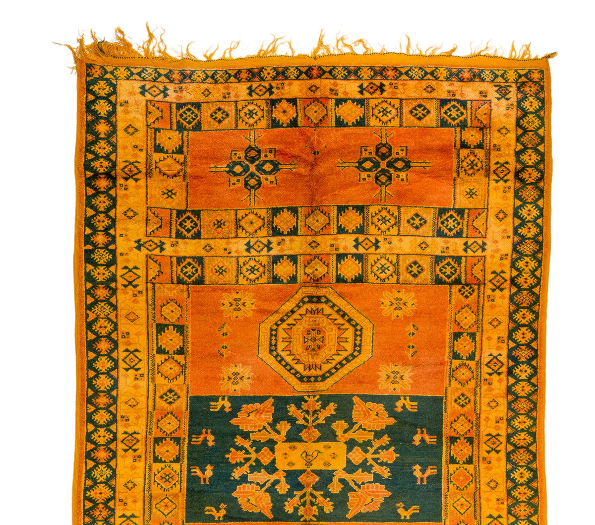 An antique-style geometric area rug with a warm orange and mustard yellow field, dark green borders, and a central teal section with ornate floral motifs and fringed edges.