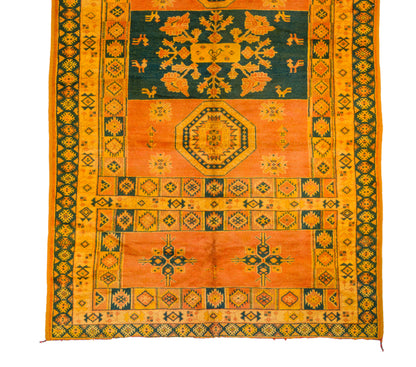 A flat-laid traditional oriental rug with a complex geometric and floral pattern, featuring a dominant orange field, a dark teal blue center, and yellow borders.