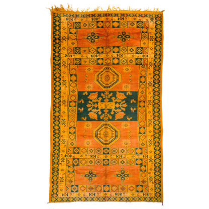 An antique-style geometric area rug with a warm orange and yellow field, dark green borders, and central medallions, shown flat against a white background.