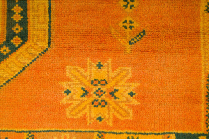 Close-up of an orange patterned rug with a central floral medallion and dark green and yellow geometric borders.
