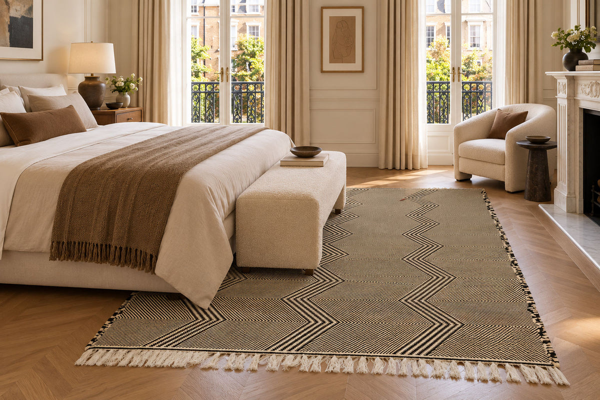 A Moroccan Zanafi rug with a beige and off-white chevron pattern and fringe tassels, styled in a bright, modern bedroom setting.