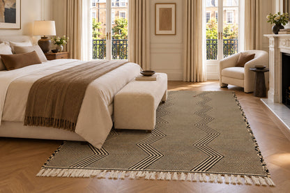 A Moroccan Zanafi rug with a beige and off-white chevron pattern and fringe tassels, styled in a bright, modern bedroom setting.