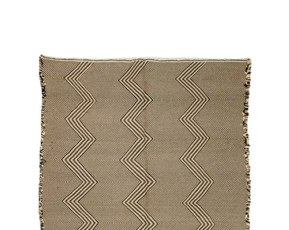 Detail of a Zanafi rug with fringe edges, featuring a beige and brown zigzag pattern on a white background.