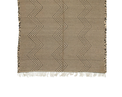 A woven Moroccan rug with a beige and brown chevron pattern and white fringe tassels, shown flat against a white background.