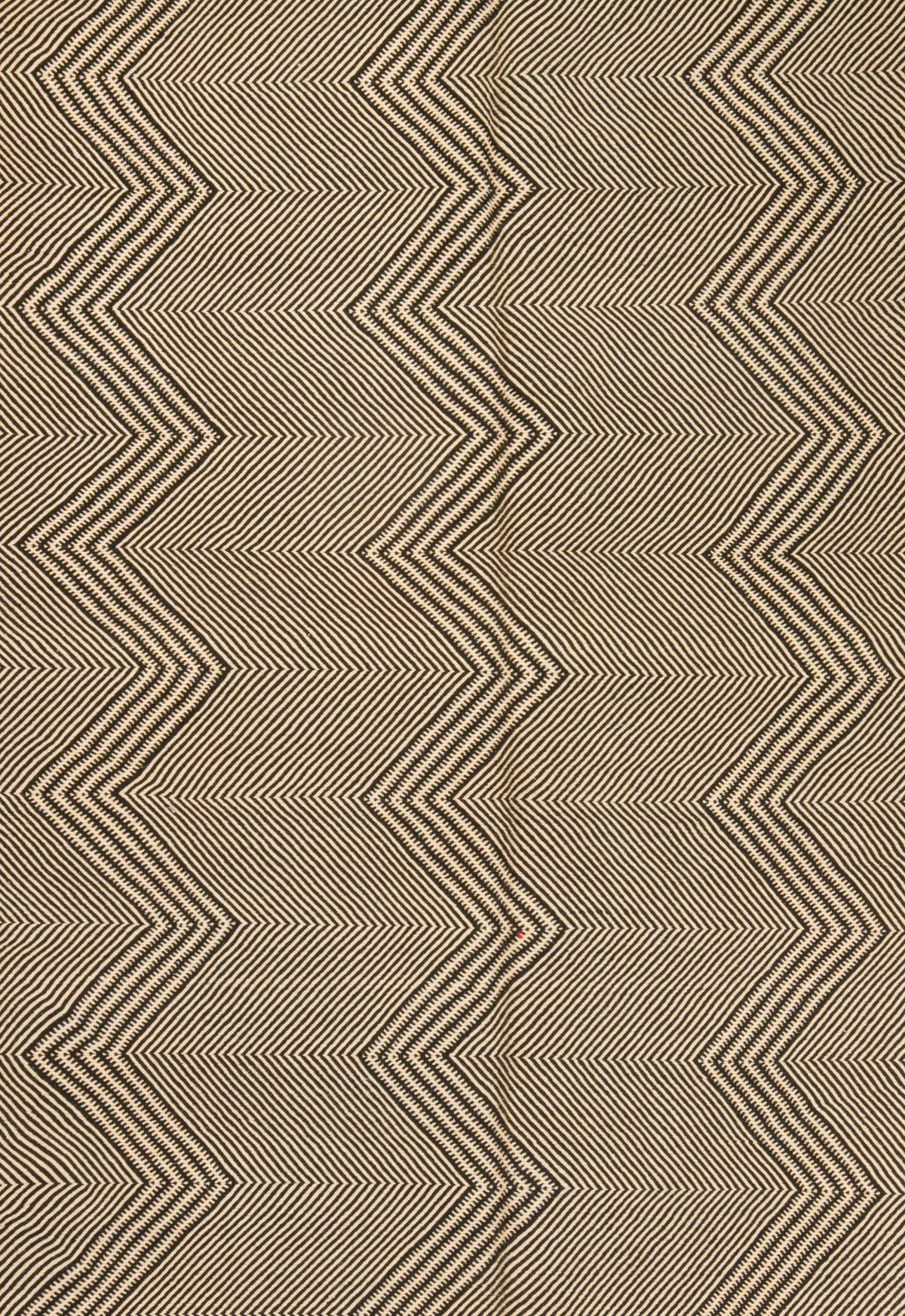 A close-up of a zigzag Zanafi rug in warm beige and brown tones, showing a repeating chevron design made of fine parallel lines.