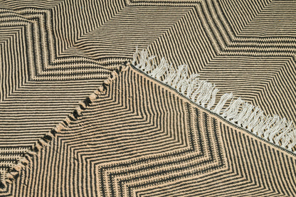 Close-up of a woven moroccan zabnafi rug with a geometric herringbone pattern in beige and black, featuring white fringe along one edge.