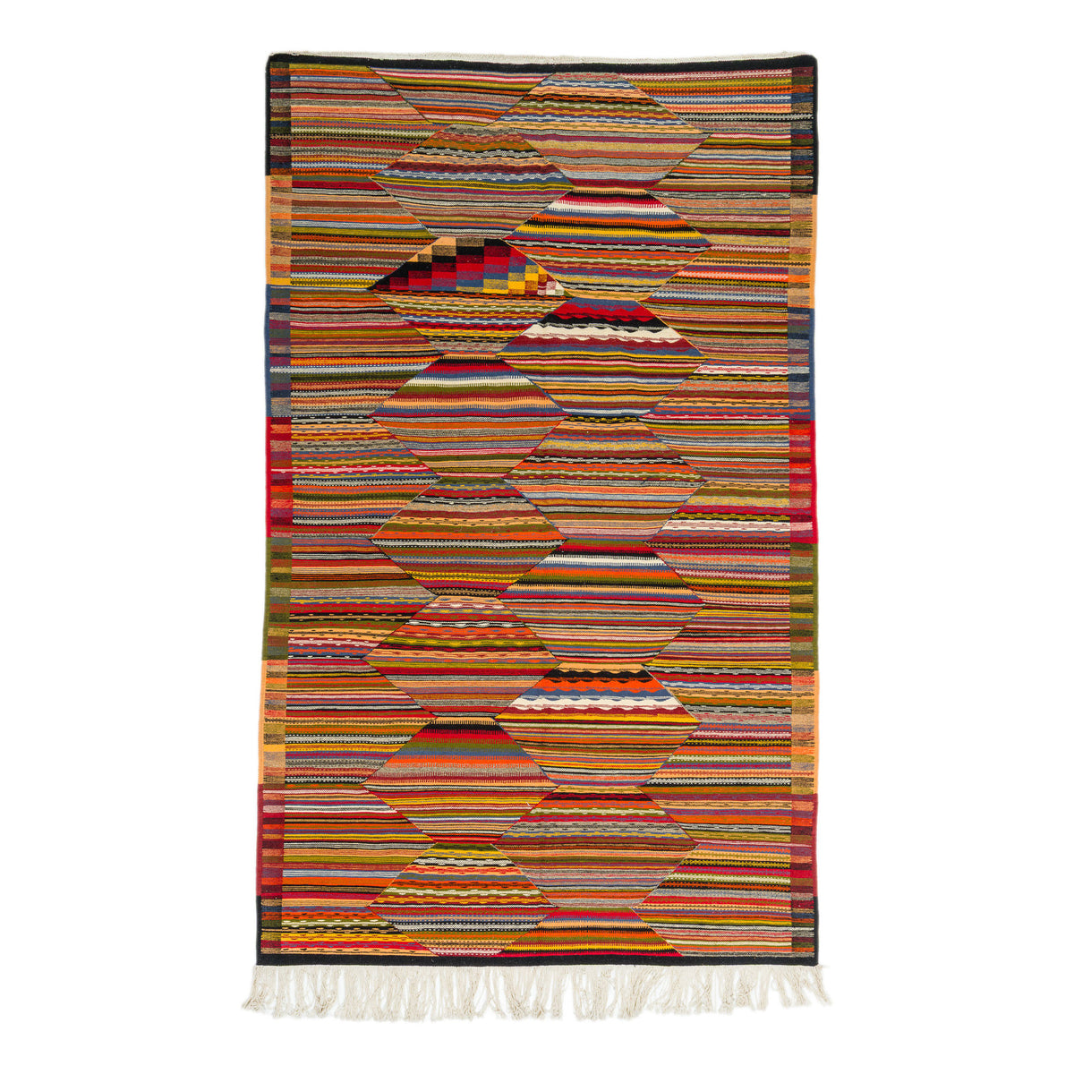 A rectangular woven Moroccan  rug with a geometric pattern made of horizontal striped textile sections in many colors, finished with white fringe along the bottom, shown on a plain white background.