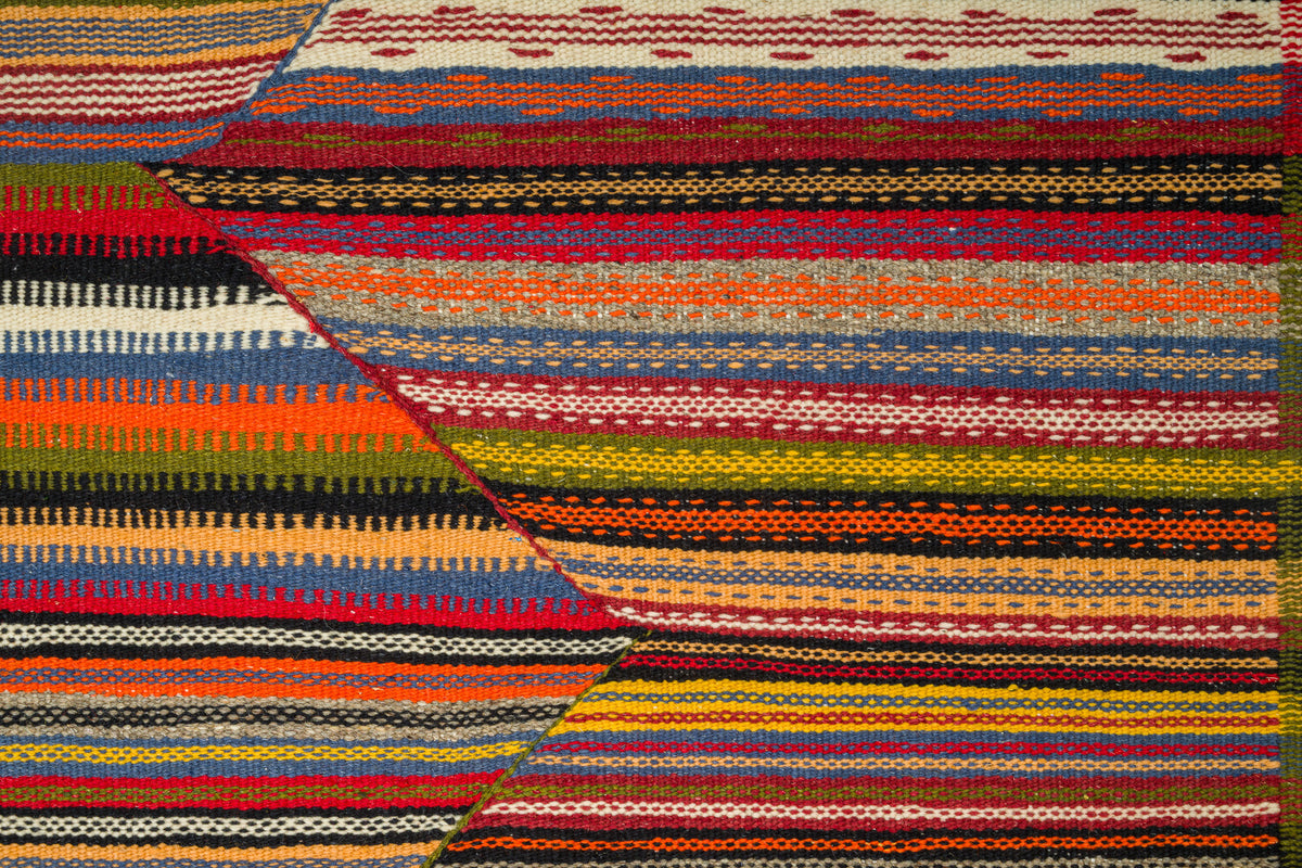 A close-up of a woven rug with bold horizontal and diagonal stripes in red, orange, yellow, green, blue, black, and cream.