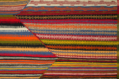 A close-up of a woven rug with bold horizontal and diagonal stripes in red, orange, yellow, green, blue, black, and cream.