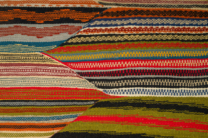 A close-up of a woven moroccan rug with horizontal and diagonal striped bands in orange, red, blue, beige, black, olive green, and brown.