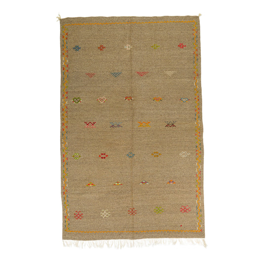 A rectangular woven Akhnif moroccan wool rug in a natural beige color, decorated with small multicolored hand embroidered geometric and floral motifs and finished with white fringe on the bottom edge, shown flat against a white background.