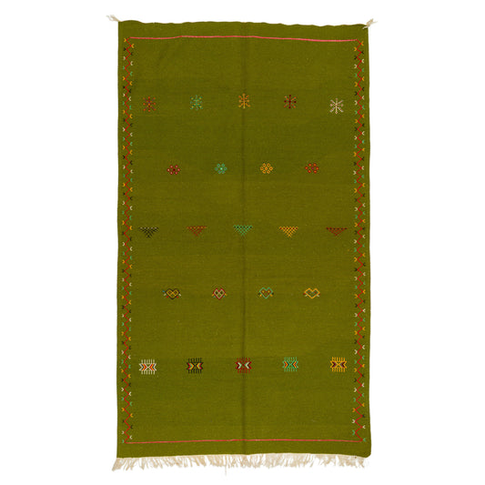 An olive green handwoven moroccan wool rug with a geometric pattern of small embroidered colored motifs and white fringe at the bottom, shown flat against a white background.