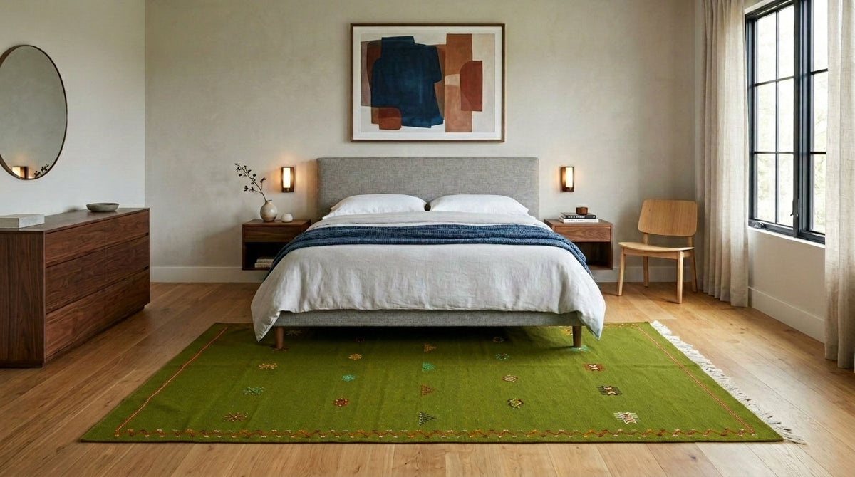 A green moroccan area rug with a subtle pattern and fringe, styled on a light wood floor in a modern bedroom setting with a bed, nightstands, and a window.