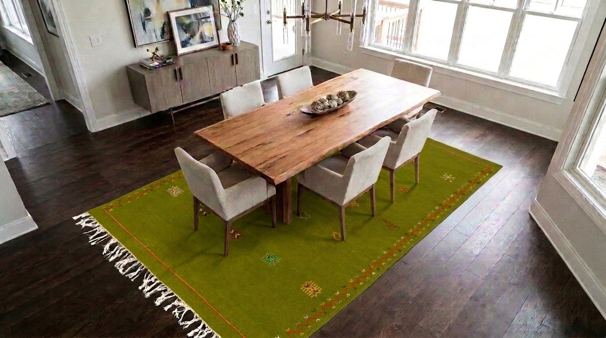 A green moroccan area rug with fringe and embroidered details under a wooden dining table and six upholstered chairs in a bright dining room.