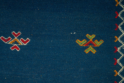 Close-up of a dark blue moroccan rug from akhnif with small geometric embroidered motifs in red, yellow, and green, plus a decorative border along the right edge.