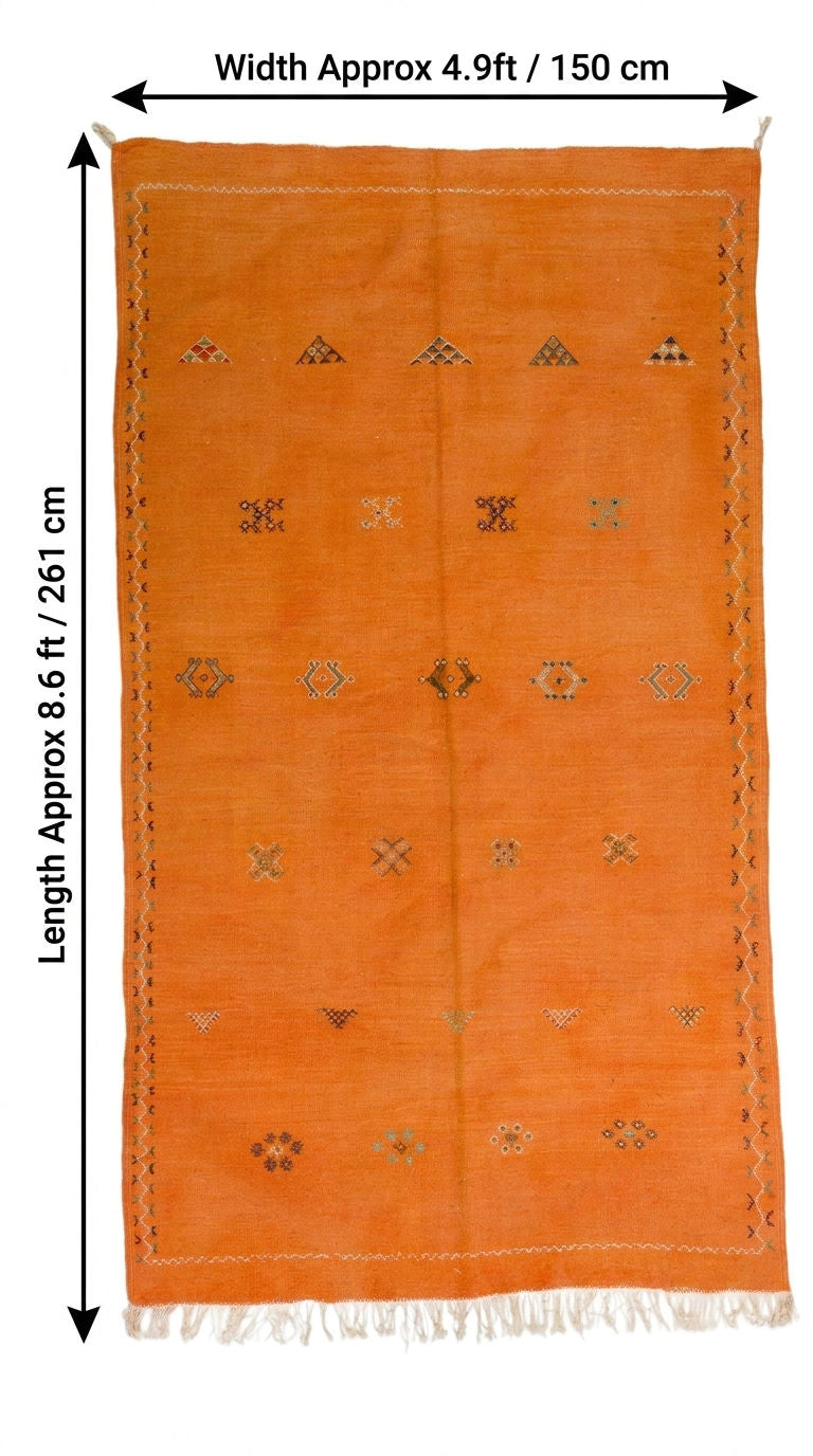 An orange rectangular moroccan rug with small embroidered geometric motifs and fringe, shown with dimension arrows and text indicating width approx. 4.