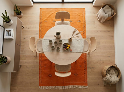 Overhead view of a bright orange moroccan rug set under dining table with cream chairs  in a bright room.