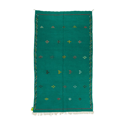 A rectangular emerald green moroccan rug handwoven with a white fringe at the bottom, decorated with small embroidered multicolored geometric motifs and bordered by a patterned edge, shown flat against a white background.