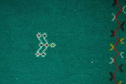 Close-up of a green moroccan rug with embroidered geometric and zigzag patterns in white, red, yellow, and black.
