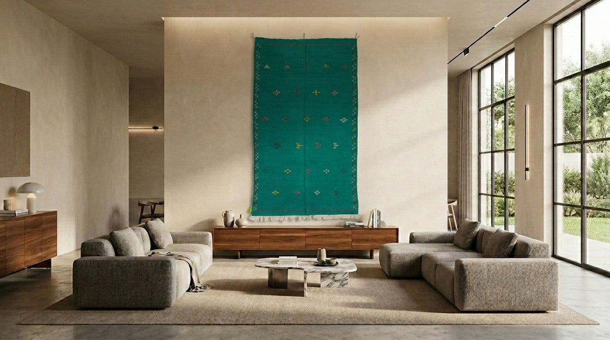 A large green moroccan rug hanging on the wall of a modern living room with two gray upholstered sofas facing a low wooden console and a round coffee table.