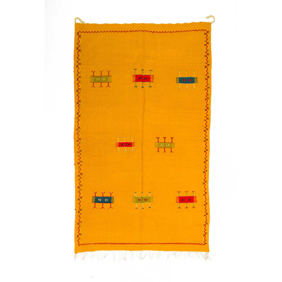 A rectangular mustard yellow moroccan rug with a hand embroidered geometric motifs in red, green, and blue, featuring a decorative border and white fringe on a white background.