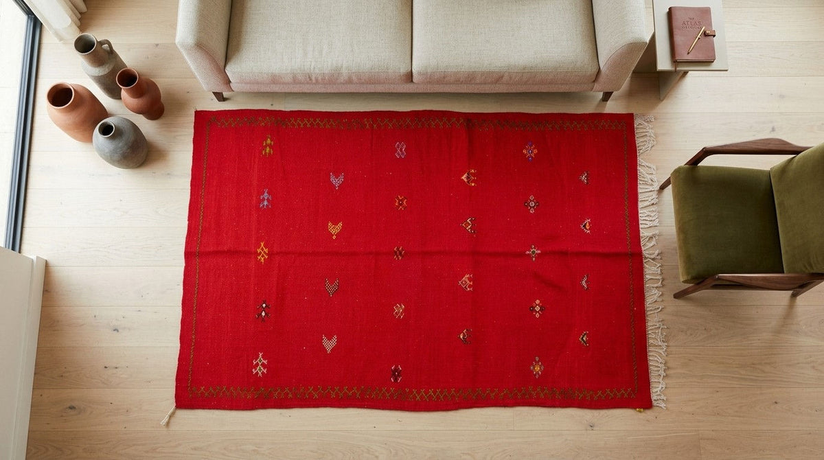 A vibrant red wool area rug with small embroidered motifs, laid out on a light wood floor in a modern living room setting.