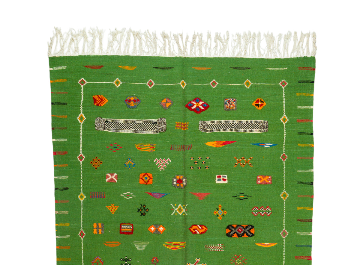 A green moroccan rug with white fringe at the top and a colorful geometric pattern, photographed against a plain white background.