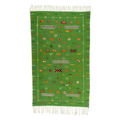 A green Moroccan rug with white fringe on the top and bottom, featuring a central field of colorful geometric patterns and a striped border.