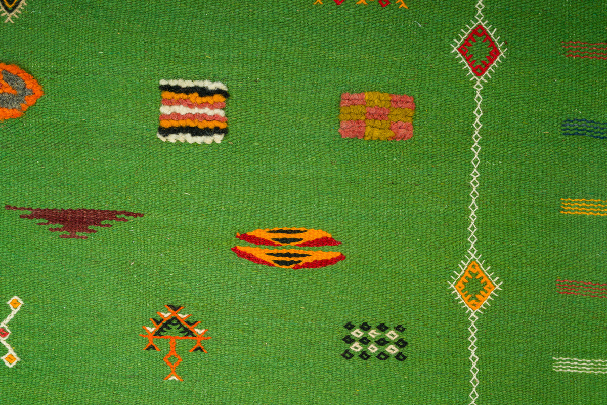 A close-up of a green Moroccan rug with scattered geometric and striped motifs in orange, red, yellow, pink, black, and white.