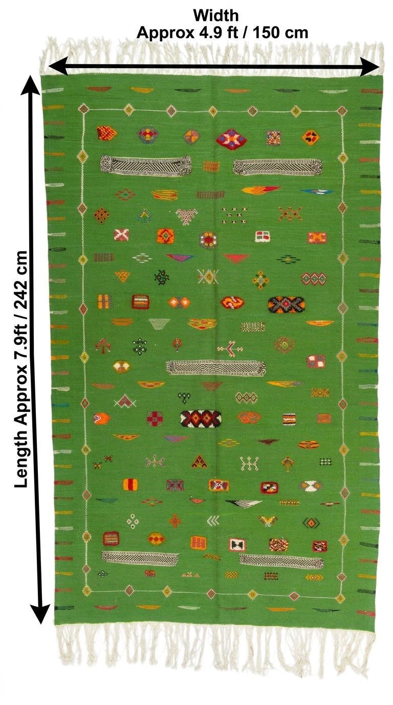 A green woven rug with white fringe on the top and bottom, decorated with colorful geometric patterns and bordered by white lines. Black arrows and text indicate dimensions.