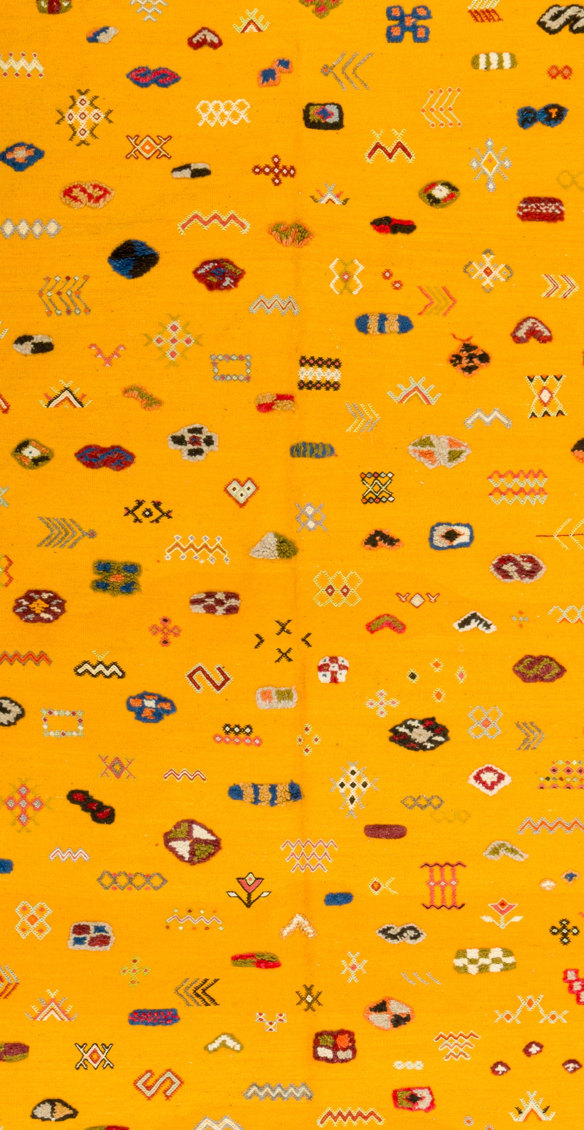 A close-up of a bright yellow rug or fabric with an all-over repeating pattern of small geometric and abstract motifs in red, blue, black, white, and brown.
