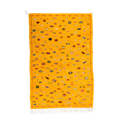 A vibrant yellow Moroccan rug with intricate multicolor geometric patterns and white fringe at the bottom, displayed flat against a white background.