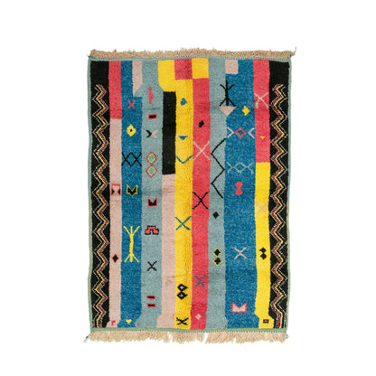 A rectangular hand knotted Moroccan rug with a multicolor geometric pattern featuring vertical stripes in blue, yellow, pink, black, and beige, finished with a fringed top and bottom edge.