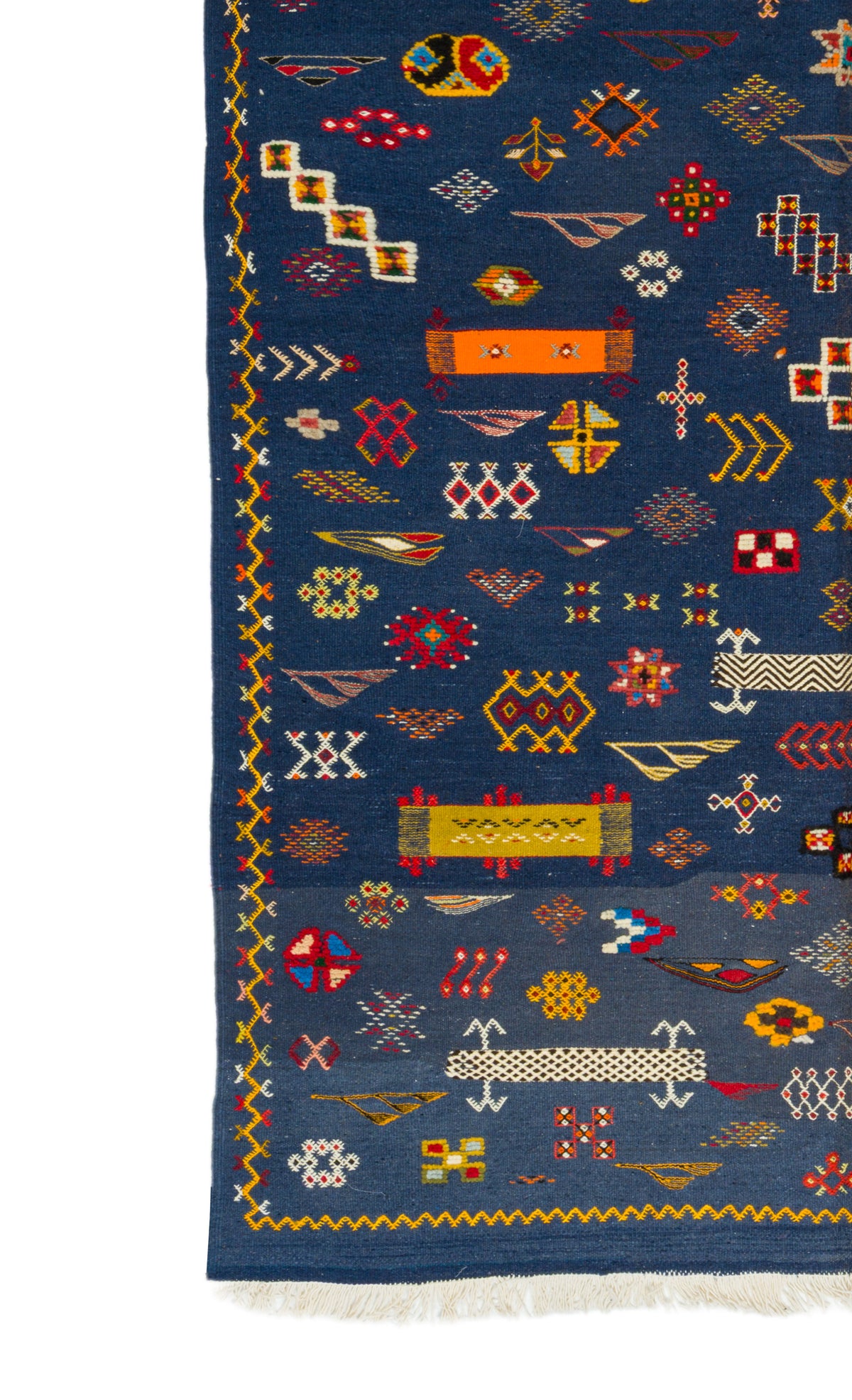 A close-up of a blue patterned rug with geometric and tribal-inspired motifs in red, yellow, white, and orange, featuring a fringed edge.