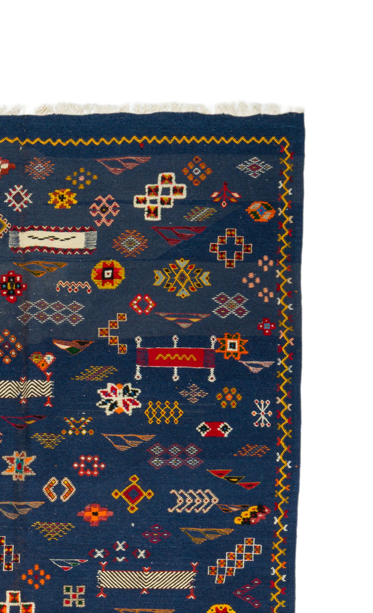 A close-up of a dark blue patterned rug with geometric motifs in red, yellow, orange, and white, showing part of the woven texture and fringe.