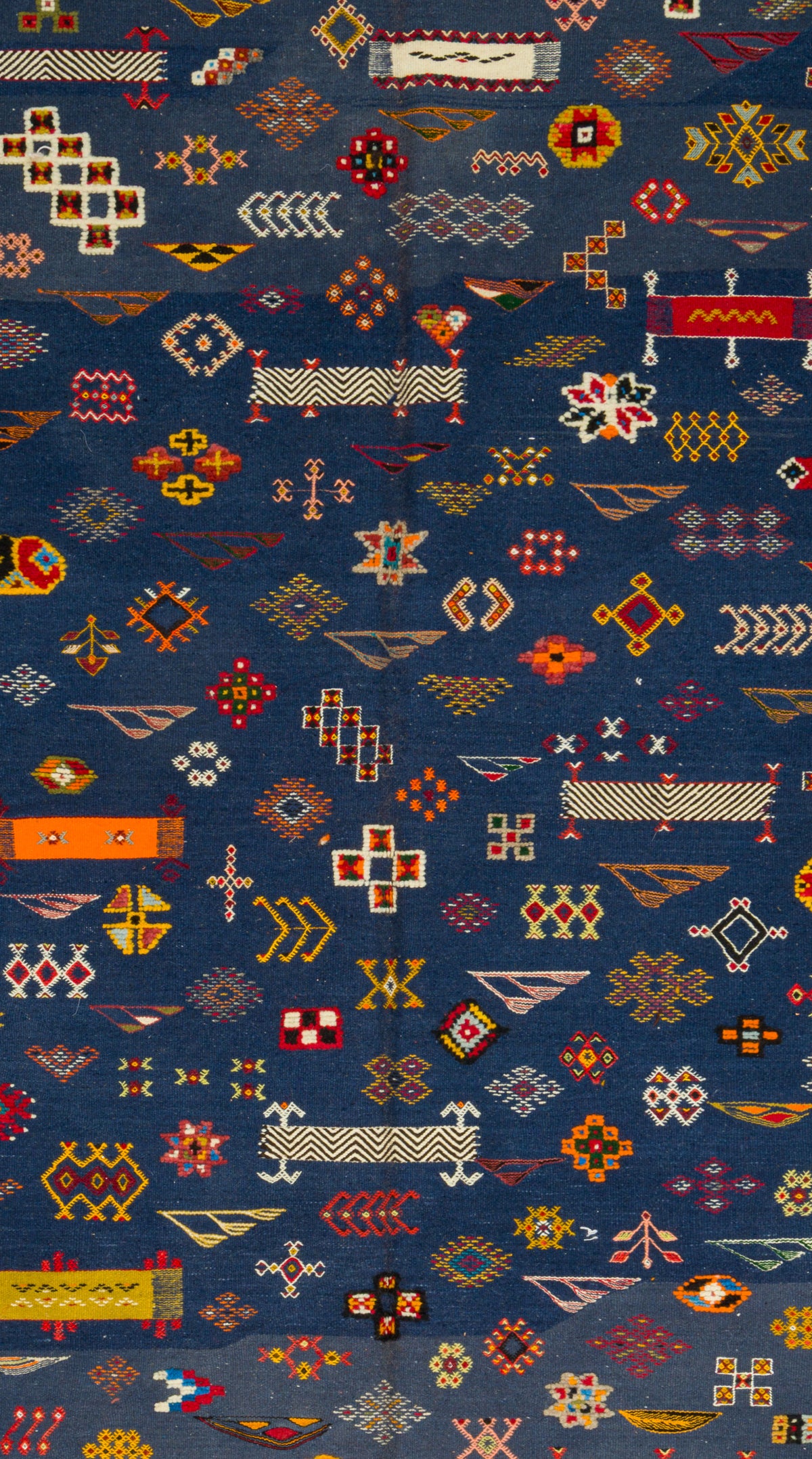 A close-up of a dark blue patterned rug featuring dense geometric and tribal-style motifs in red, orange, yellow, white, and beige.
