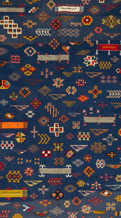 A close-up of a dark blue patterned rug featuring dense geometric and tribal-style motifs in red, orange, yellow, white, and beige.