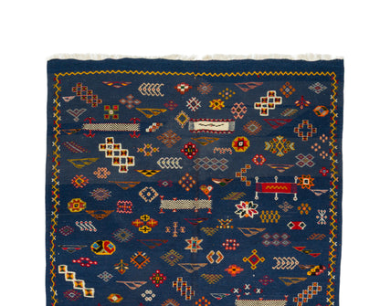 A dark blue woven rug with intricate multicolor geometric patterns and a fringed edge, shown flat against a white background.