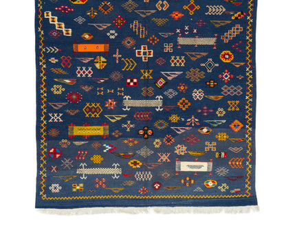 A dark blue wool rug with intricate multicolor geometric patterns and white fringe along the bottom edge, shown flat against a white background.