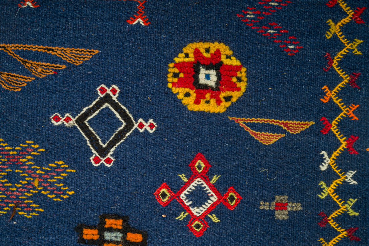 Close-up of a rug with a dark blue background and geometric Southwestern-style motifs in red, yellow, orange, white, and black.