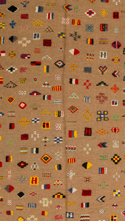 A close-up of a moroccan rug with a tan background and an all-over pattern of small geometric and tribal-style motifs in red, yellow, black, white, and blue.