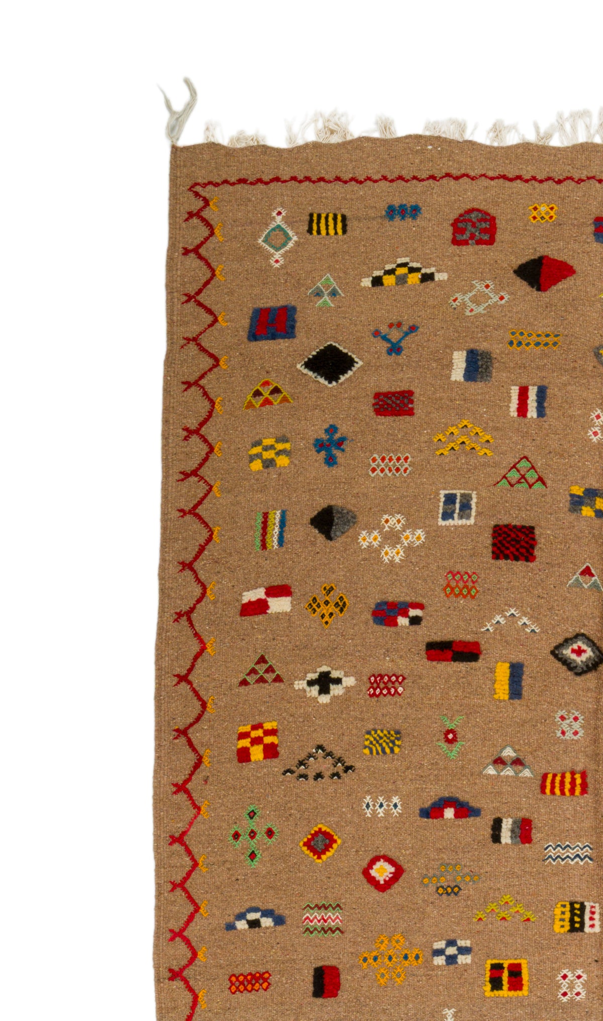 A close-up of a woven rug with a tan background, featuring a colorful geometric pattern of small flags and symbols, a red zigzag border, and white fringe at the top.