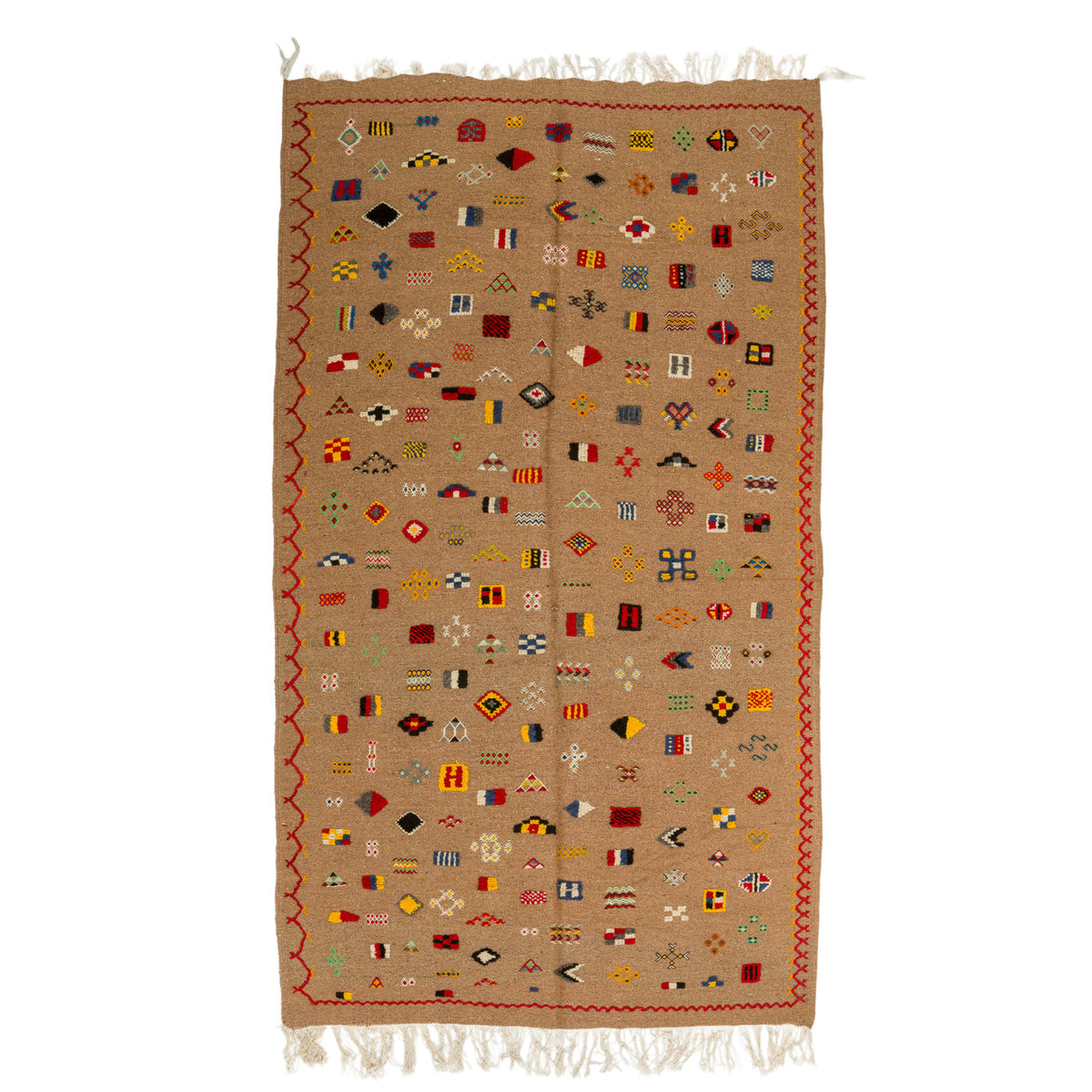A rectangular woven rug with a tan base and a dense array of small multicolored geometric motifs, finished with white fringe on the top and bottom edges.