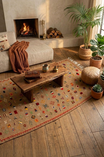 A bohemian-style area rug with a multicolor geometric pattern on a beige background, styled in a cozy living room with a fireplace, wooden coffee table, and potted plants.