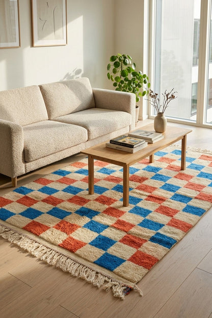 A colorful checkered area rug with cream, blue, and terracotta red squares, styled in a bright modern living room with a beige sofa and a wooden coffee table.