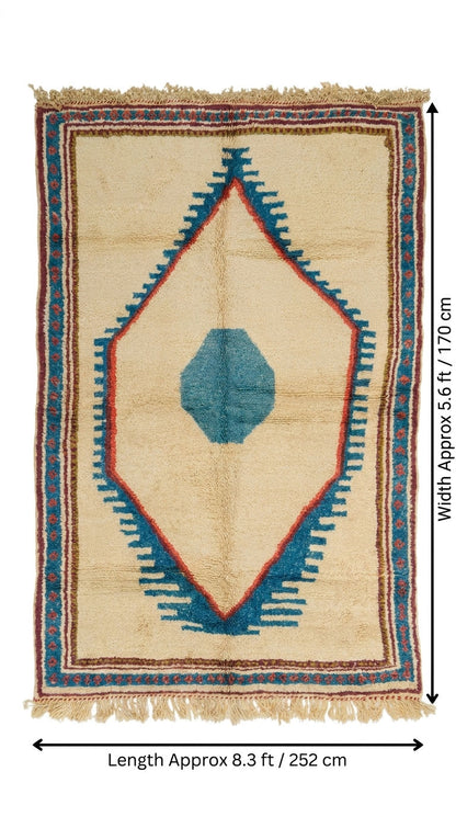 A flat-laid woven rug with a cream base, featuring a large blue geometric diamond motif with red and blue accents, and fringed edges. Black dimension lines and text indicate a length of approximately 8.