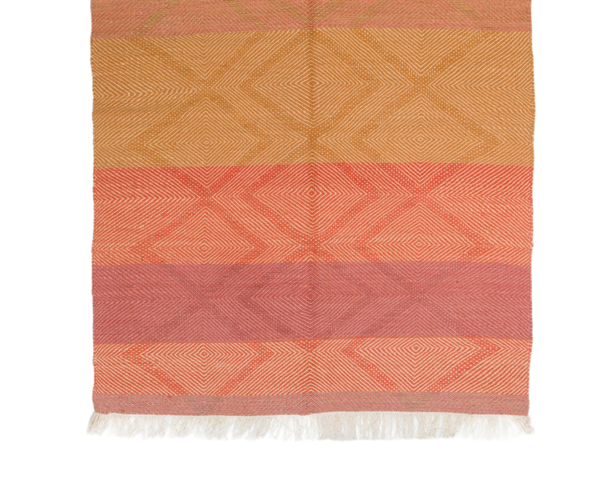 A rectangular woven moroccan rug with horizontal stripes in warm orange, coral, and muted pink tones, featuring a subtle geometric diamond pattern and white fringe along the bottom edge, shown against a plain white background.