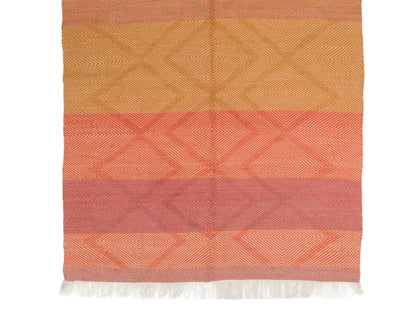 A rectangular woven moroccan rug with horizontal stripes in warm orange, coral, and muted pink tones, featuring a subtle geometric diamond pattern and white fringe along the bottom edge, shown against a plain white background.
